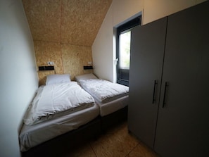 Ein kleines, kompaktes Zimmer mit zwei Einzelbetten, einem Fenster mit Jalousien und einem Kleiderschrank.