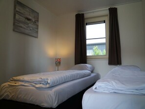 Een kamer met twee bedden, een raam met gordijnen, een wandlamp en een schilderij.
