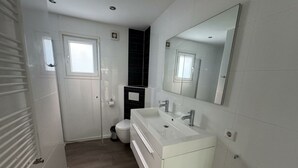 Un baño moderno con tocador blanco, dos lavamanos, inodoro y ducha.