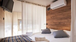 A hotel room with a bed, a TV, an air conditioner, and a window with curtains. - Glamping Tent Luxe 4 (Kaatsheuvel)