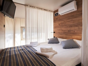 Ein Hotelzimmer mit Bett, Fernseher, Klimaanlage und einem Vorhangfenster.