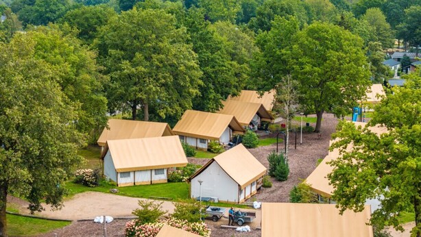 A campsite with multiple tents and a small building, surrounded by dense trees. - Glamping Tent Luxe 4 (Kaatsheuvel)
