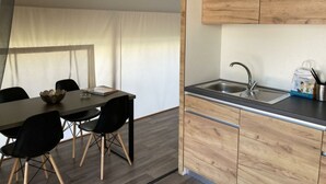 A modern kitchen with wooden cabinets, a sink, and a dining area with chairs and a table. - Glamping Tent Luxe 4 (Kaatsheuvel)