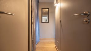 Een smalle gang met houten vloer, een spiegel aan de muur en een deur met een handgreep aan de rechterkant.