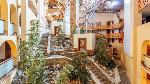 Een atrium met meerdere niveaus, een centrale trap, stenen muren en houten leuningen.