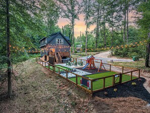 Une cabane avec une terrasse, une balançoire et un toboggan.