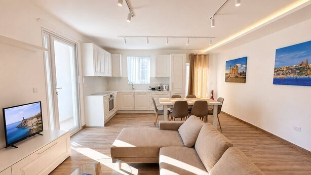 Un salon moderne comprenant un canapé, une table basse en verre, un téléviseur et un coin repas avec des chaises et une table.