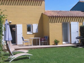 A yellow building with a tiled roof, a patio with chairs and a table, and a small garden area. - The Amareyeurs (Le Château-d'Oléron)