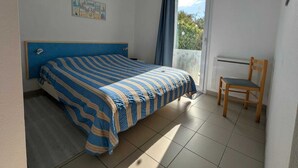 Un dormitorio con cama, una silla, una ventana con cortinas y un cuadro en la pared.
