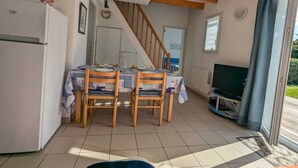 Un comedor con una mesa dispuesta para cuatro personas, sillas de madera, un refrigerador, un televisor y una escalera que sube a otra habitación.