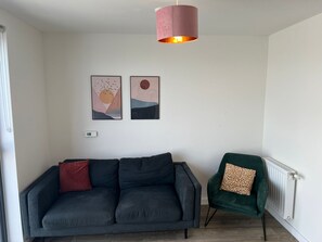 Een moderne woonkamer met een donkergrijze bank, een groene fauteuil en twee abstracte kunstwerken aan de muur.