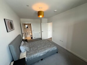 Een slaapkamer met een bed, nachtkastje, lamp, spiegel en een deur naar de badkamer.