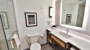 Ein modernes Badezimmer mit Toilette, Waschbecken und großem Spiegel. Ein gerahmtes Bild ist an der Wand und ein Handtuchhalter vorhanden.
