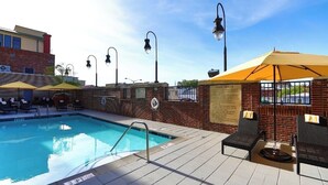 Ein Swimmingpool mit Liegestühlen und Sonnenschirmen, eine Backsteinmauer und ein Schild mit Regeln.