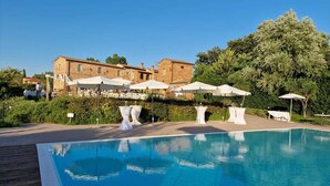 Un espace piscine avec une terrasse en bois, des parasols blancs et un bâtiment en arrière-plan.