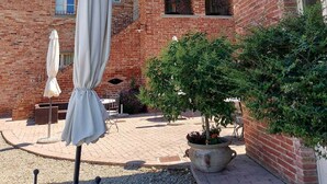 Une cour avec un bâtiment en briques, un espace extérieur abrité avec des sièges, et un pot de fleurs.