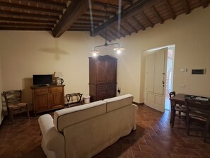 Un salon comprenant un canapé, un meuble en bois, une télévision et un coin repas avec une table et des chaises.