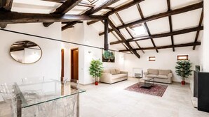 Uma sala de estar ampla com teto alto, uma mesa de jantar de vidro, dois sofás e plantas em vasos.