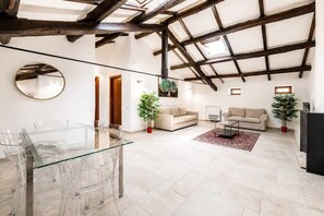 A spacious living area with a high ceiling, a glass dining table, two sofas, and potted plants. - Rooftop Terraces with Volcano & Castles Views (8) (Naples)