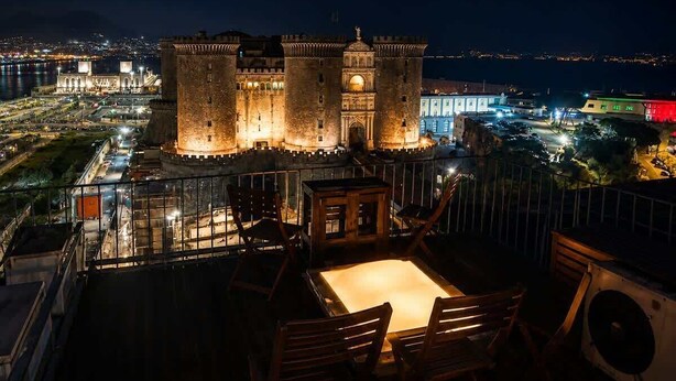 Un bâtiment qui ressemble à un château, avec une tour ronde, entouré d’une clôture, et une table avec des chaises au premier plan.