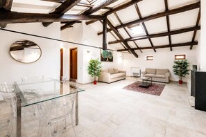 A spacious living area with a high ceiling, wooden beams, a glass dining table, two sofas, and potted plants. - Naples Penthouse with Rooftop Castles Views (Naples)