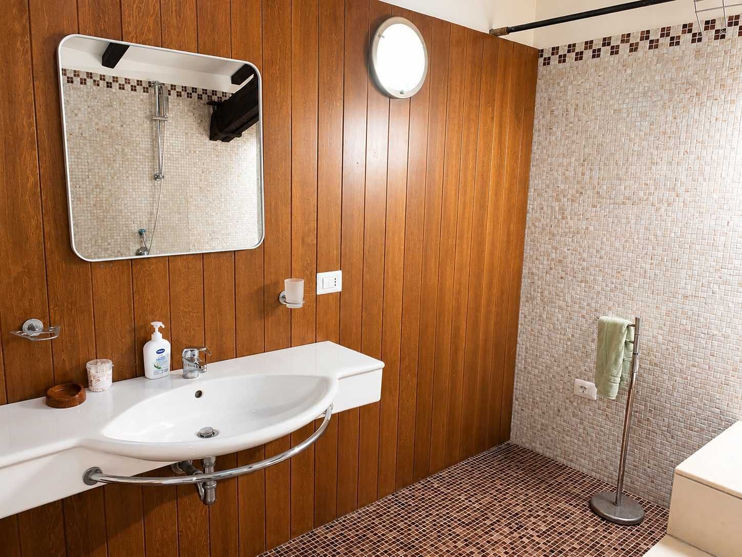 Ein Badezimmer mit einer Holzwand, einem weißen Waschbecken mit Chromarmatur, einem Spiegel, einem Handtuchhalter und einer Duschkabine mit Mosaikfliesen.