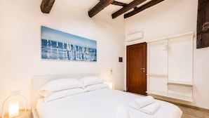 Une chambre avec un grand lit, un tableau représentant des voiliers, une porte en bois et une armoire blanche.