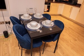 A dining table set with white plates, silverware, and wine glasses, surrounded by blue chairs in a modern kitchen with wooden flooring. - Luxury 2Bed 2Bath City Centre Apt | Balcony View (Leeds)