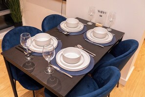 Een eettafel gedekt met witte borden, kommen, bestek en wijnglazen, omringd door blauwe stoelen.
