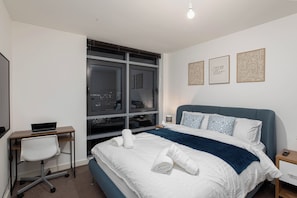 Ein Hotelzimmer mit Bett, Schreibtisch, Stuhl, Nachttisch und Fenster mit Blick auf die Stadt.