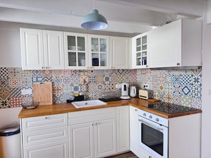 Eine Küche mit weißen Schränken, einer farbenfrohen Fliesenrückwand, einer Holz Arbeitsplatte, einer Spüle, einem Schneidebrett, einem Wasserkocher, einem Toaster und einem Backofen.