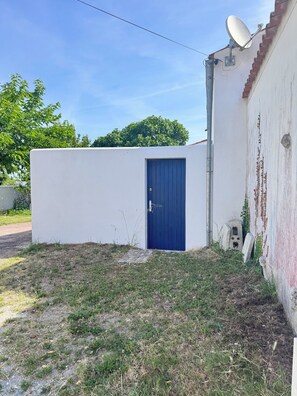 Un bâtiment blanc avec une porte bleue, une antenne parabolique et un bloc de béton.
