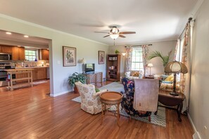A spacious living area with a kitchen, a ceiling fan, a television, and a bookshelf.