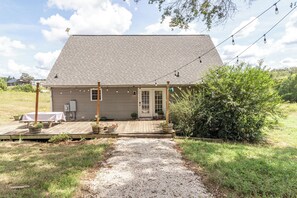 A single-story house with a sloped roof, a front porch with a table and chairs, and a gravel driveway leading to the entrance.