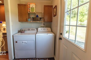 A laundry room with two stacked washers and dryers, wooden cabinets above, and a window with a view of greenery.