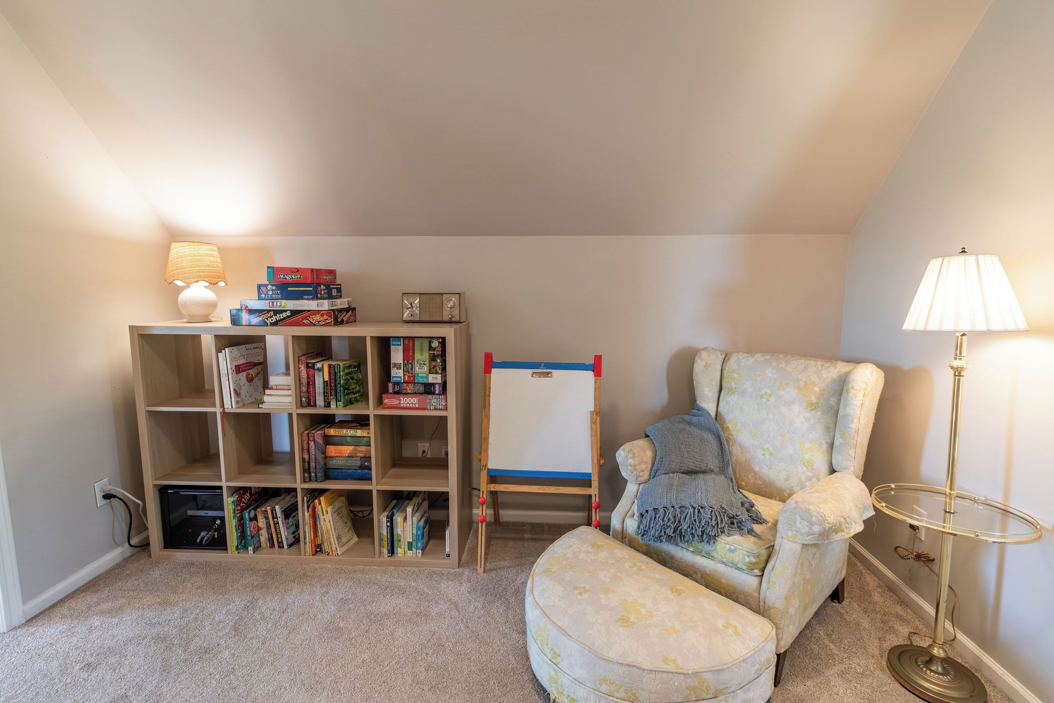 Un coin lecture confortable avec un fauteuil moelleux, une petite table d’appoint, une bibliothèque remplie de livres et un tableau blanc.
