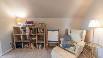 Un coin lecture confortable avec un fauteuil moelleux, une petite table d’appoint, une bibliothèque remplie de livres et un tableau blanc.