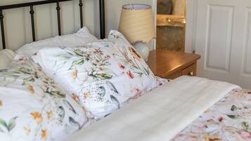 Un letto con lenzuola a motivi floreali, una lampada da comodino e un comodino in legno.