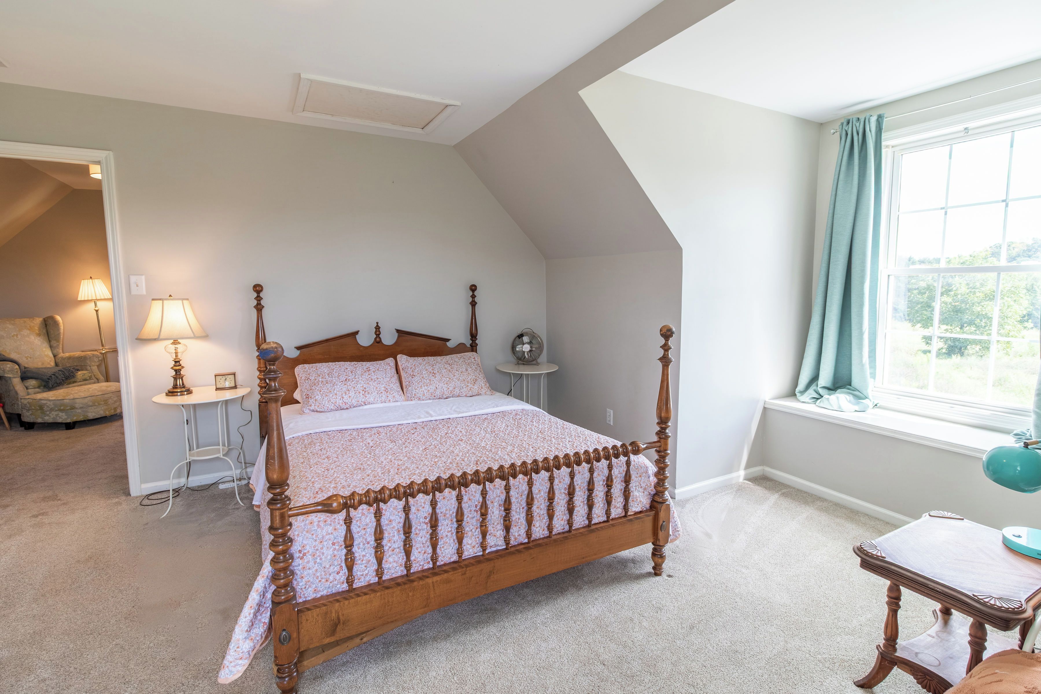 Un dormitorio con una cama con dosel, una zona de estar con una silla y una mesa, y una ventana con cortinas.