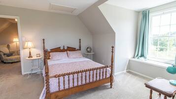 Un dormitorio con una cama con dosel, una zona de estar con una silla y una mesa, y una ventana con cortinas.
