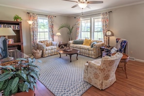 A living room with floral-patterned furniture, a ceiling fan, and a bookshelf.