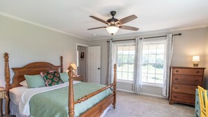 Ein Schlafzimmer mit Himmelbett, Deckenventilator, Kommode und einem fenster mit Vorhängen.