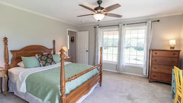 Une chambre à coucher avec un lit à baldaquin, un ventilateur de plafond, une commode et une fenêtre avec des rideaux.