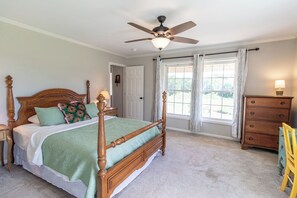 Quarto com cama de dossel, ventoinha no teto, cômoda e janela com cortinas.