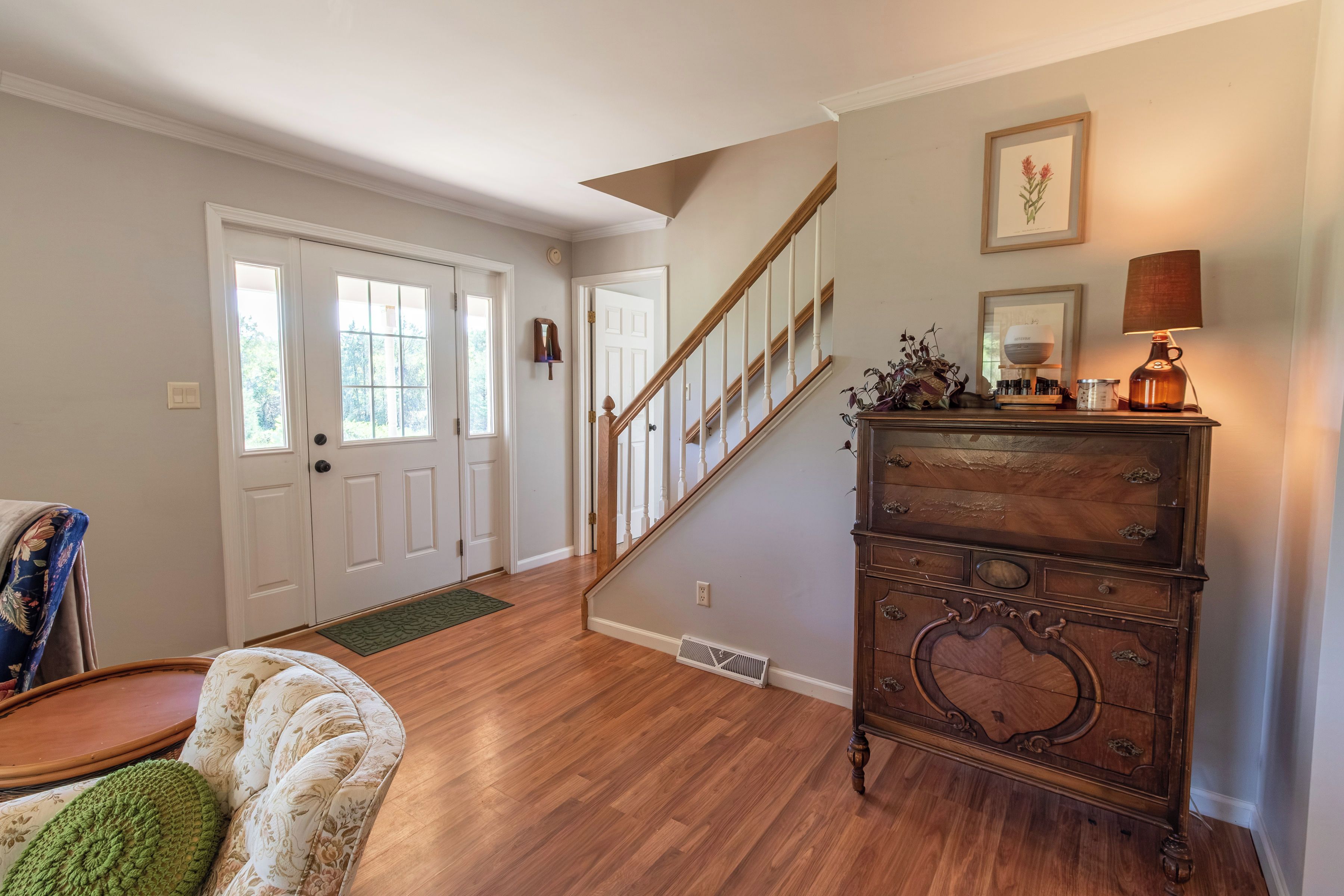 A spacious living room with hardwood flooring, a staircase, and a wooden dresser with decorative items.