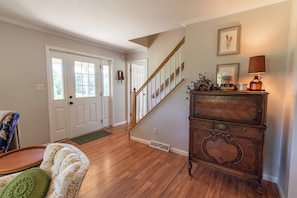 A spacious living room with hardwood flooring, a staircase, and a wooden dresser with decorative items.