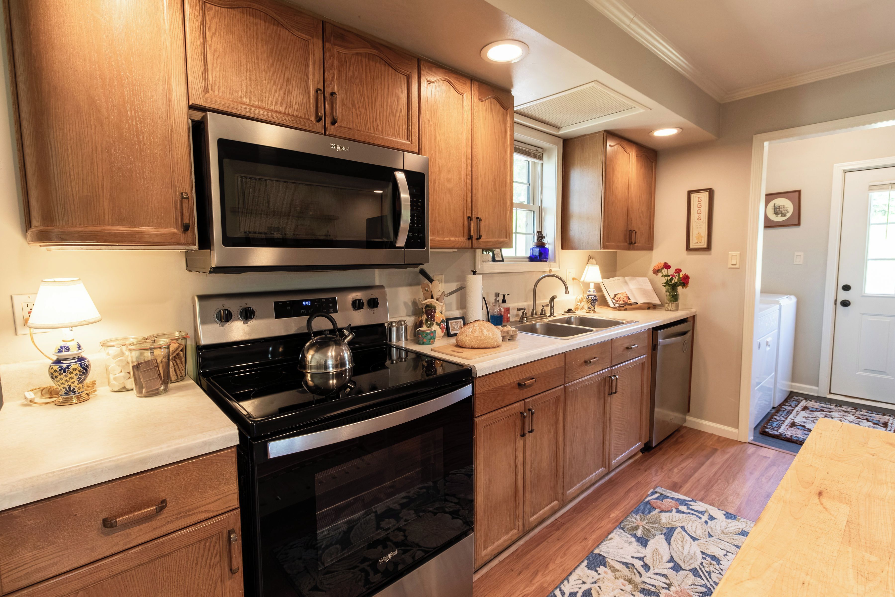 A kitchen with wooden cabinets, a stainless steel microwave, an oven, a kettle, and a sink.