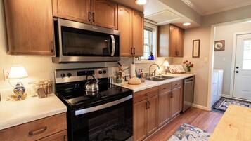 A kitchen with wooden cabinets, a stainless steel microwave, an oven, a kettle, and a sink.