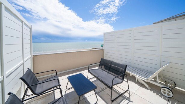 Ein Balkon mit Meerblick, ausgestattet mit einem Tisch, zwei Stühlen und einer kleinen Bank.