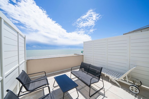 A balcony with a view of the sea, featuring a table, two chairs, and a small bench. - A comfortable 53-square-meter apartment, perfect for four people, located on the third floor (Scala A) of a building with an elevator (NOT suitable for people with disabilities) directly facing the seafront.The property is located in Lignano Sabbiadoro i (Lignano Sabbiadoro)
